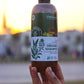 Hand holding an organic shampoo bottle with a blurred outdoor background