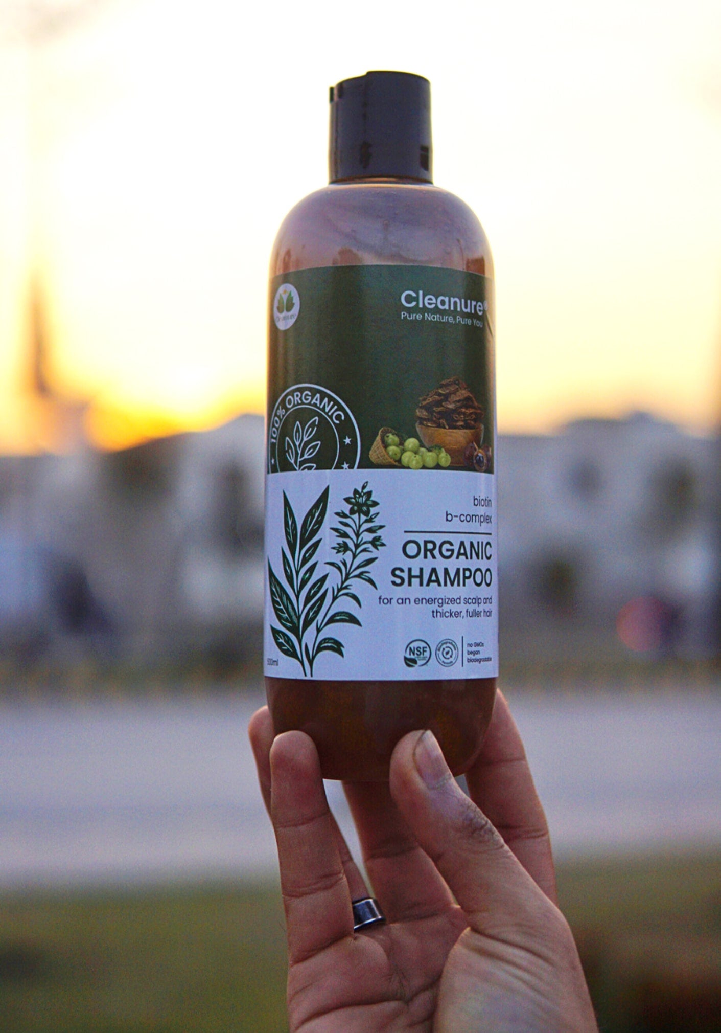 Hand holding an organic shampoo bottle with a blurred outdoor background
